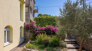 A building with a stone facade, a small garden with flowering plants, and a metal fence. - Beautiful Apartment Red Close to the Beach (Kraljevica)