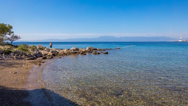 A clear coastal beach with rocky shoreline, calm water, and distant mountains. - Beautiful Apartment Red Close to the Beach (Kraljevica)