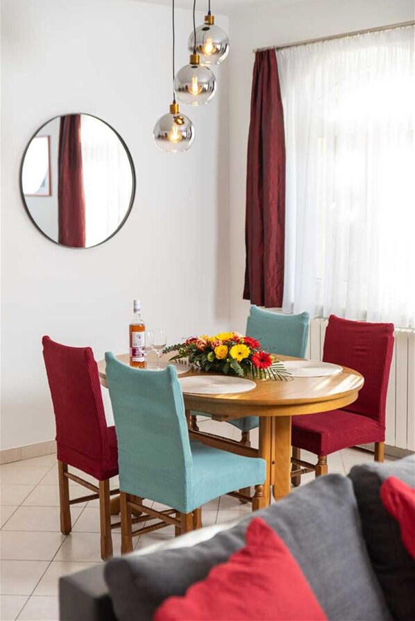 Un coin repas avec une table ronde, quatre chaises, un miroir et des lampes suspendues.