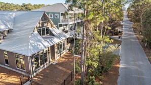 A residential area with a two-story house featuring a balcony, a driveway, and a row of trees. - Newly Built Lux Grayton Beach Home "Timeless 30A" Pool, Golf Cart, Bikes (Santa Rosa Beach)