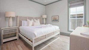 Ein Schlafzimmer mit Bett, Nachttischen, einem Schreibtisch, einem Deckenventilator und einem Fenster mit Jalousien.