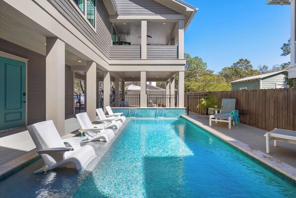A swimming pool with lounge chairs, a covered deck, and a wooden fence.