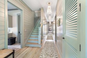 A hallway with a staircase, wooden flooring, and a patterned rug.
