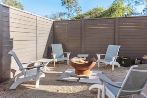 An outdoor seating area with a fire pit, white chairs, and a wooden fence. - Newly Built Lux Grayton Beach Home "Timeless 30A" Pool, Golf Cart, Bikes (Santa Rosa Beach)