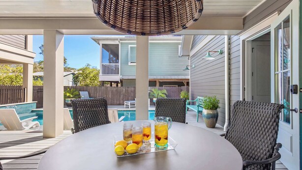 Eine Terrasse im Freien mit einem Tisch für zwei Personen, ausgestattet mit einem Eisteekrug und Zitronen, umgeben von Korbstühlen.