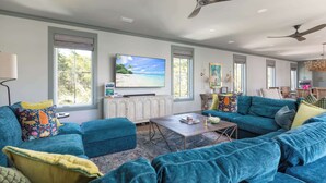 Ein geräumiges Wohnzimmer mit großem Fernseher, platzgrünen Sofas und einem Deckenventilator.