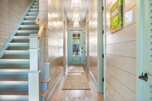 A hallway with a staircase, a door, and a hanging light fixture.