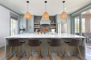 A modern kitchen with a large island, pendant lights, and bar stools.