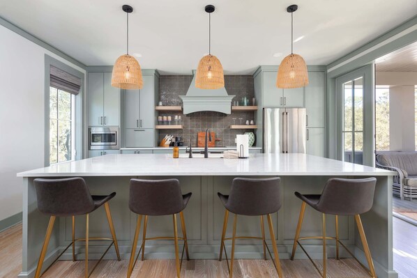 A modern kitchen with a large island, pendant lights, and bar stools.