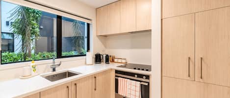 Una cocina moderna con armarios de madera, un lavamanos de acero inoxidable y un ventanal con vistas a la vegetación.