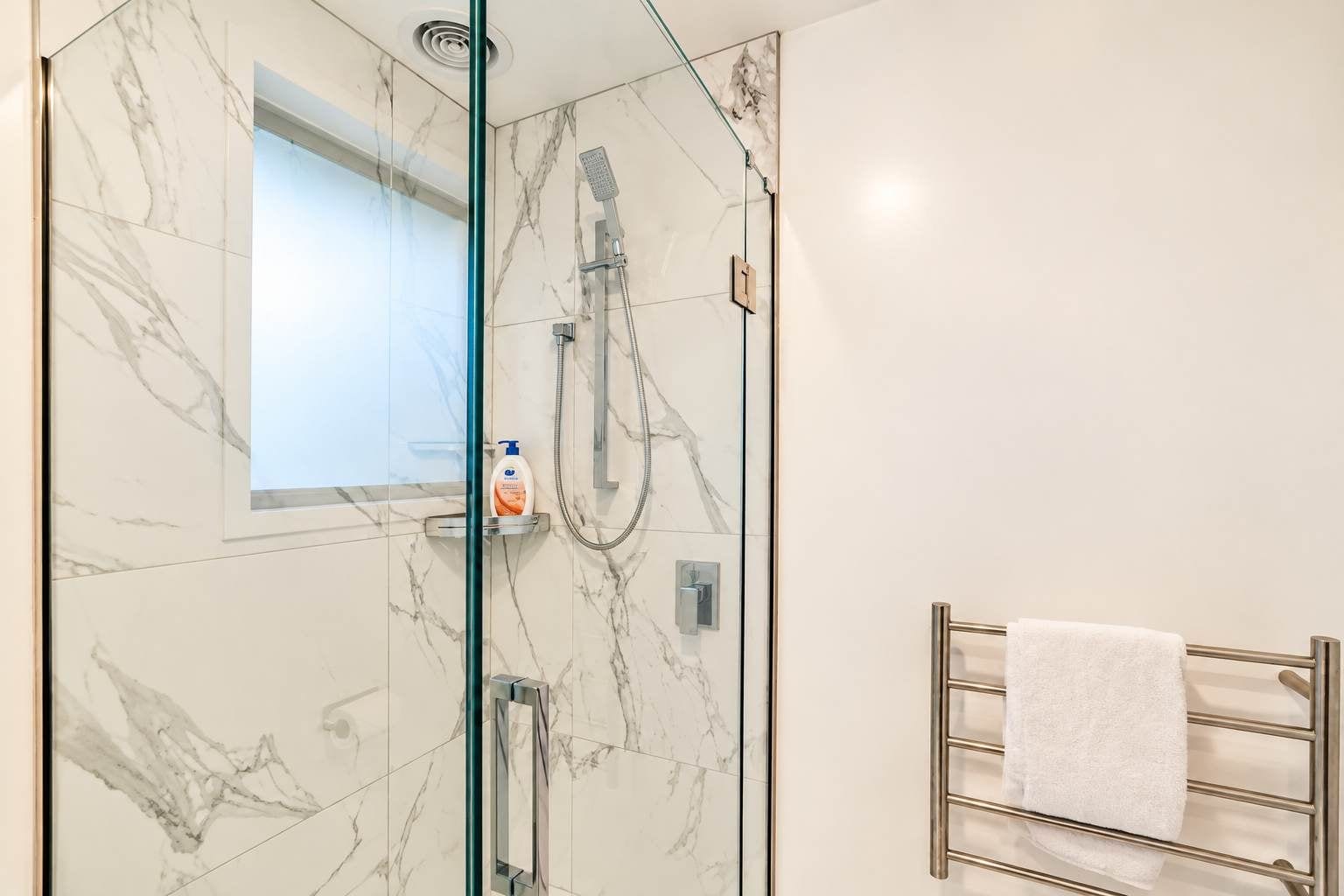 Un baño moderno con ducha envuelta en vidrio, paredes de mármol y un perchero para toallas.