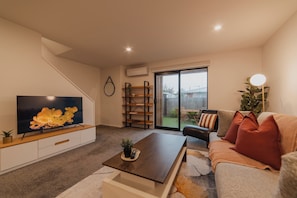 A modern living room with a flat-screen TV, a coffee table, a sofa, and a bookshelf.