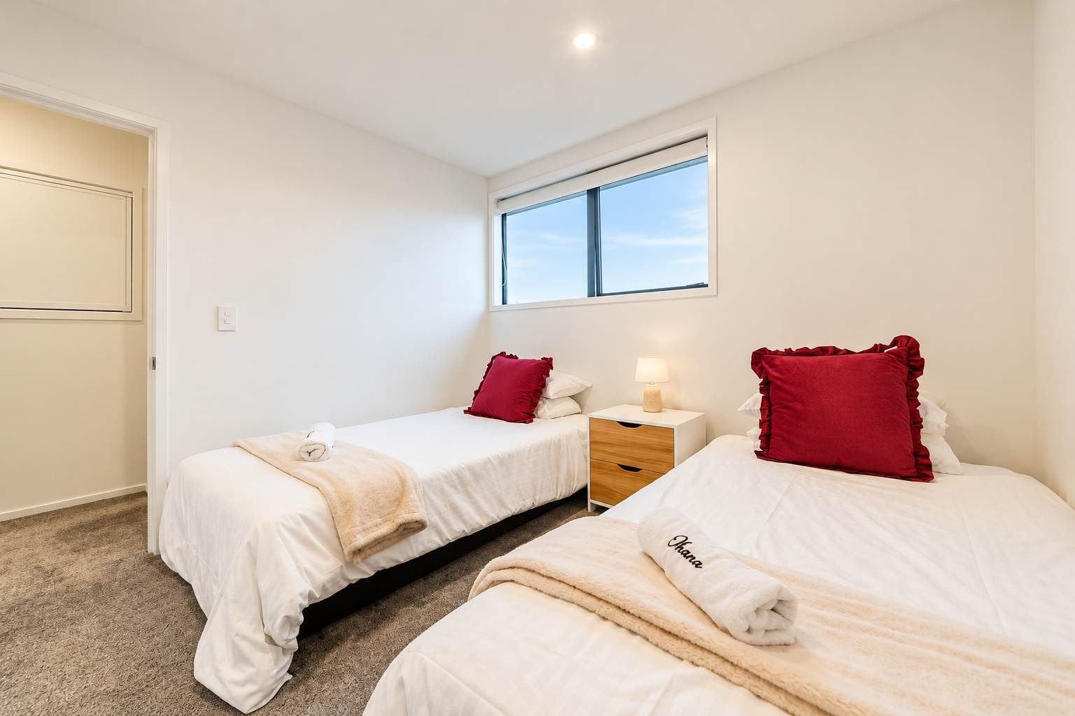 Una habitación de hotel con dos camas, una ventana, una mesita de noche y piso alfombrado.