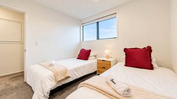 Una habitación de hotel con dos camas, una ventana, una mesita de noche y piso alfombrado.