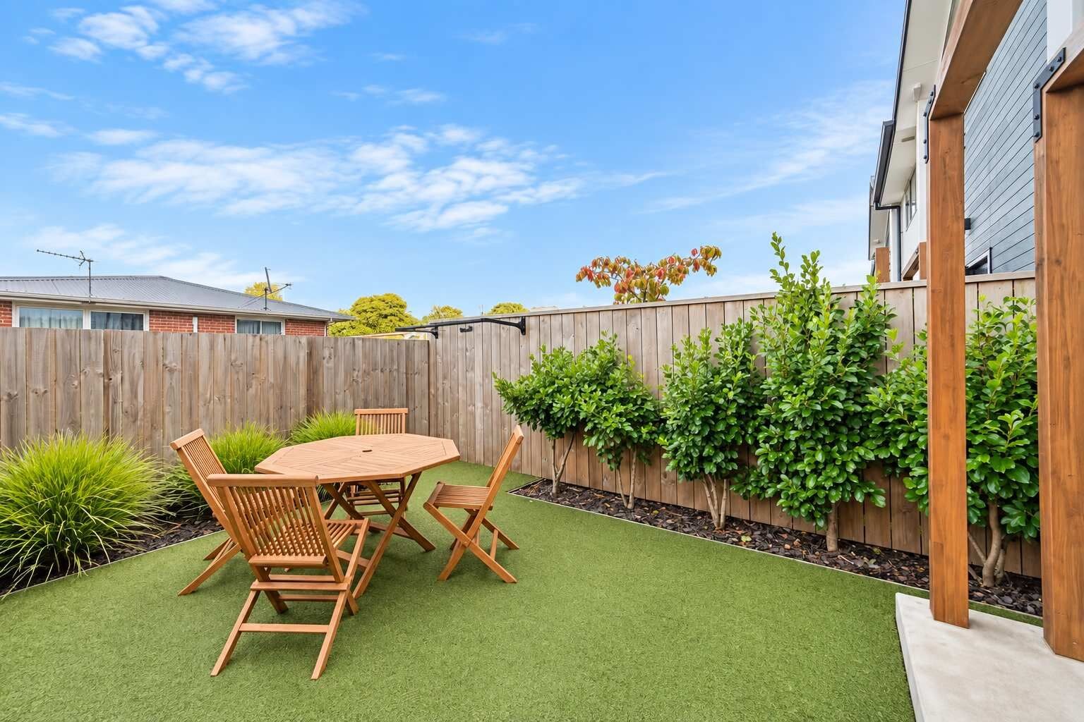 A backyard with a wooden table and chairs, surrounded by green artificial turf and a wooden fence.