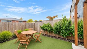 A backyard with a wooden table and chairs, surrounded by green artificial turf and a wooden fence.