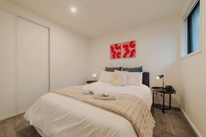 Ein ordentlich eingerichtetes Schlafzimmer mit einem Bett, zwei Nachttischen und einem Fenster.