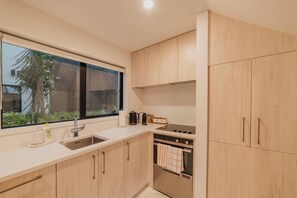 A modern kitchen with wooden cabinets, a stainless steel sink, and a window overlooking greenery.