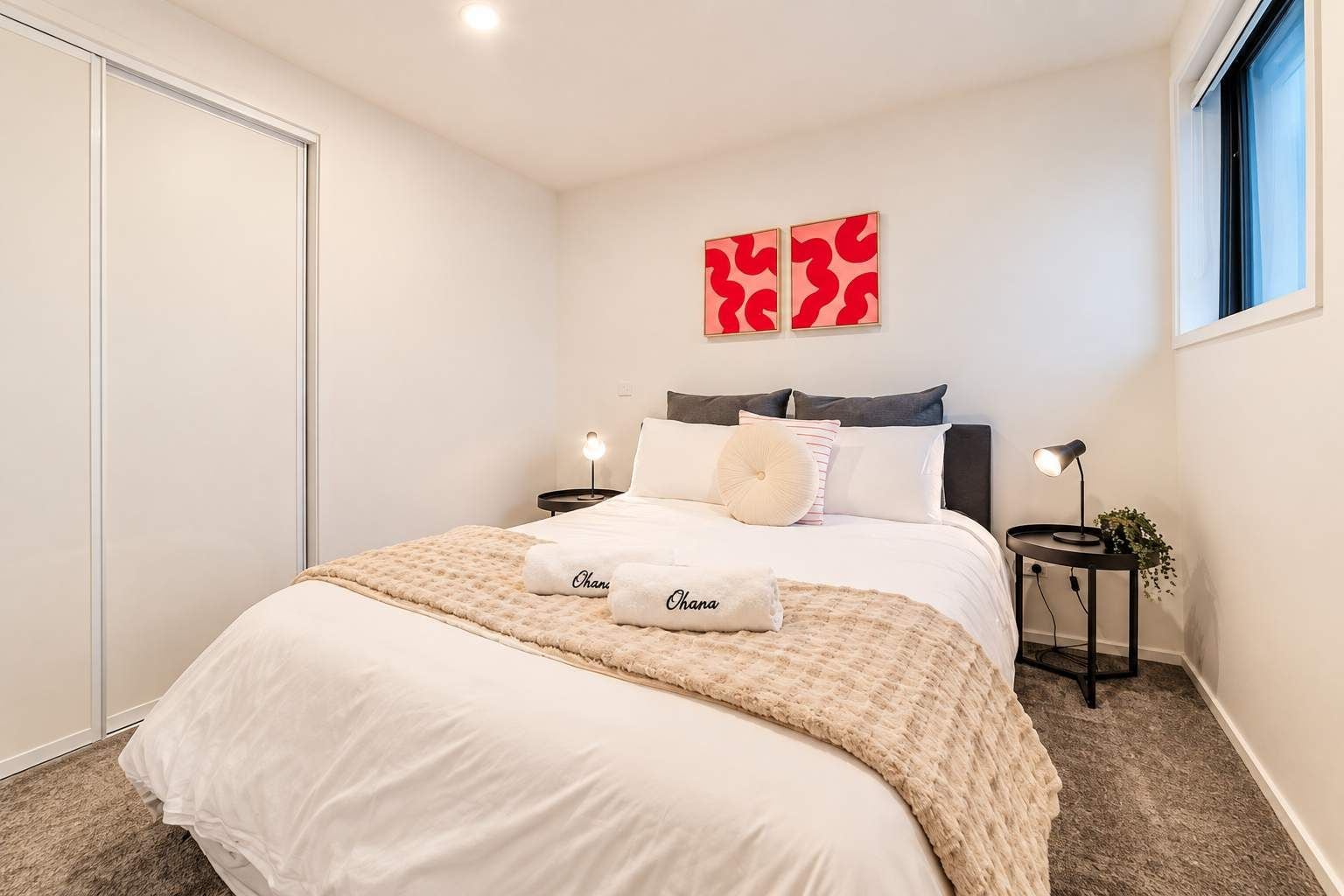 Un dormitorio con cama, almohadas, una mesita de noche, una lámpara y una ventana.