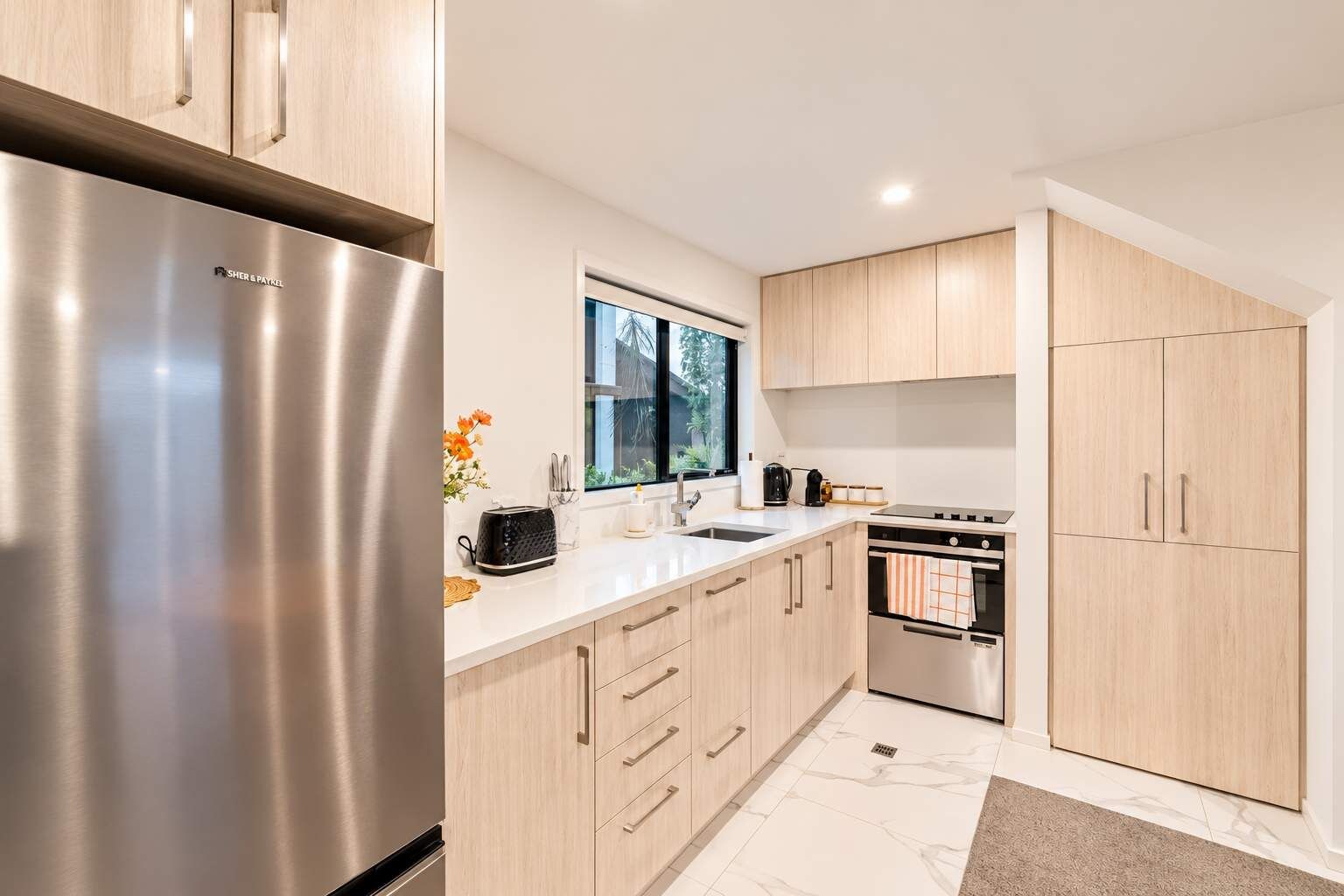 Una cocina moderna con electrodomésticos de acero inoxidable, armarios de madera y un ventanal que proporciona luz natural.