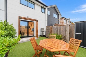 Et moderne hus med en patio, et træbord med stole og en lukket baghave.