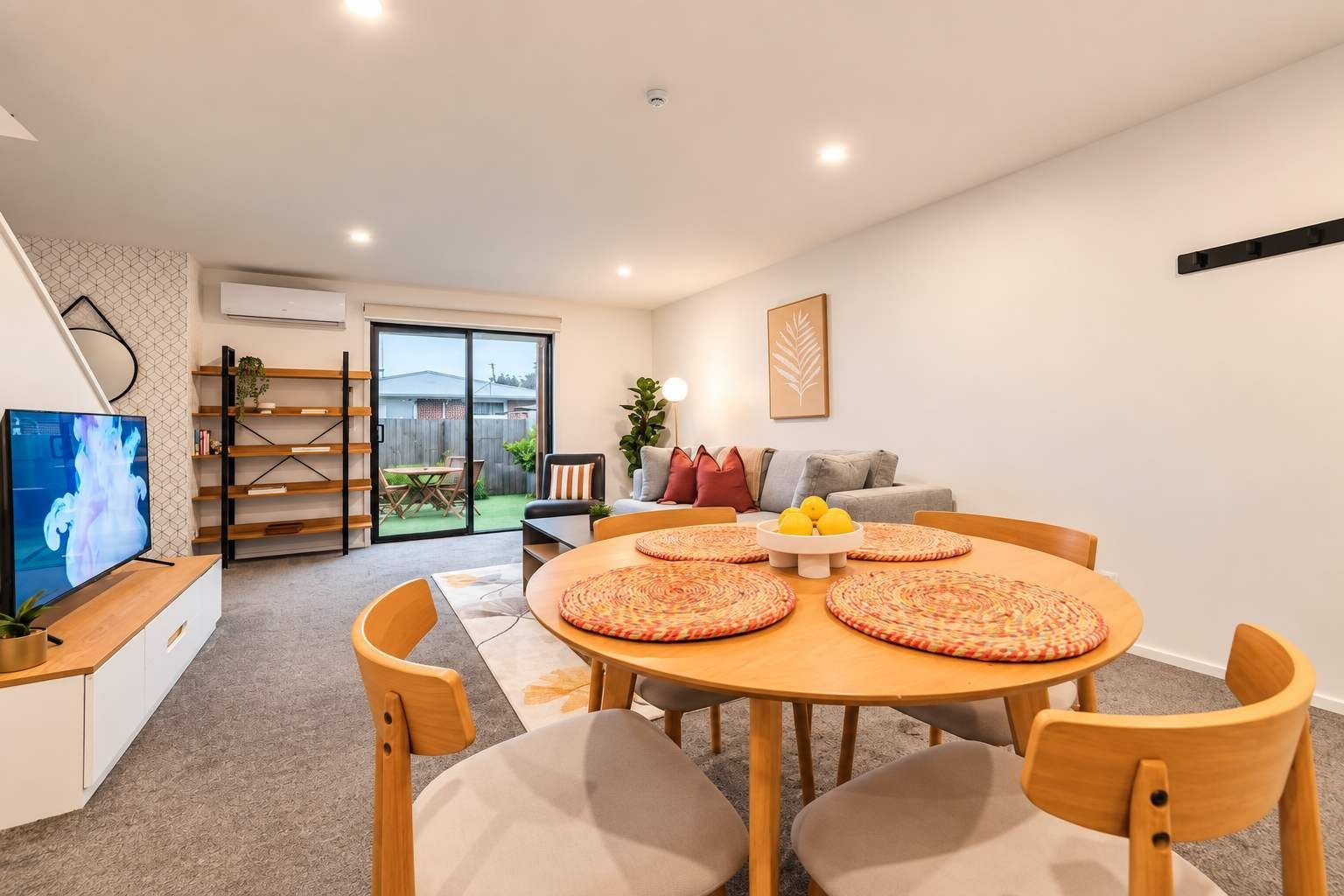 Una sala de estar moderna con comedor, televisor de pantalla plana y puerta corrediza de vidrio que da a un patio.