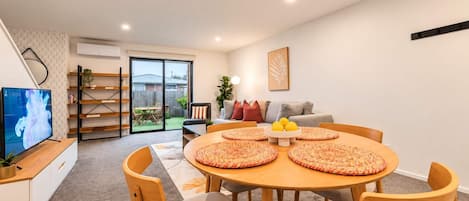 Una sala de estar moderna con comedor, televisor de pantalla plana y puerta corrediza de vidrio que da a un patio.
