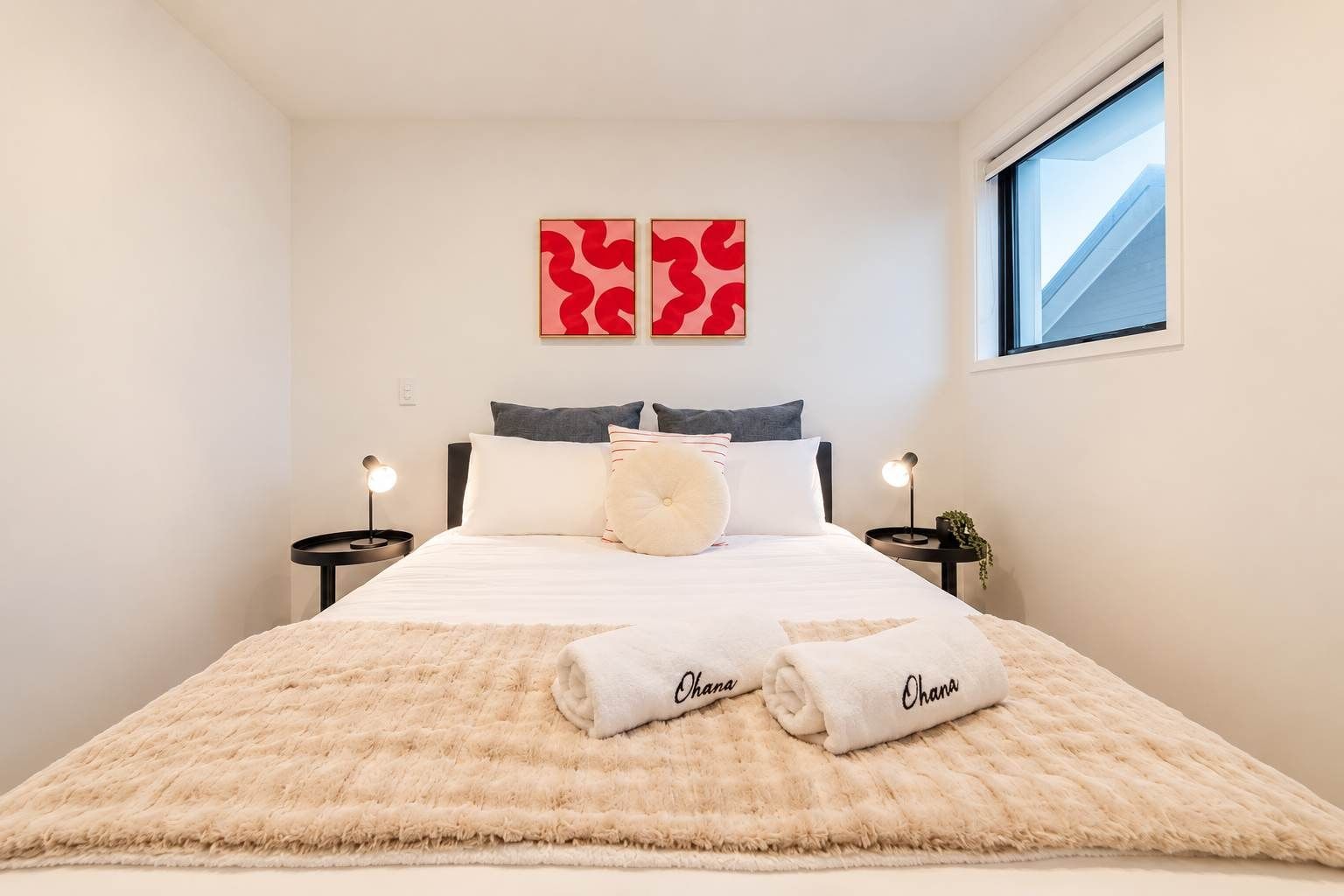 A hotel room with a bed, two bedside tables, a window, and two wall-mounted artworks.