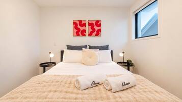 A hotel room with a bed, two bedside tables, a window, and two wall-mounted artworks.