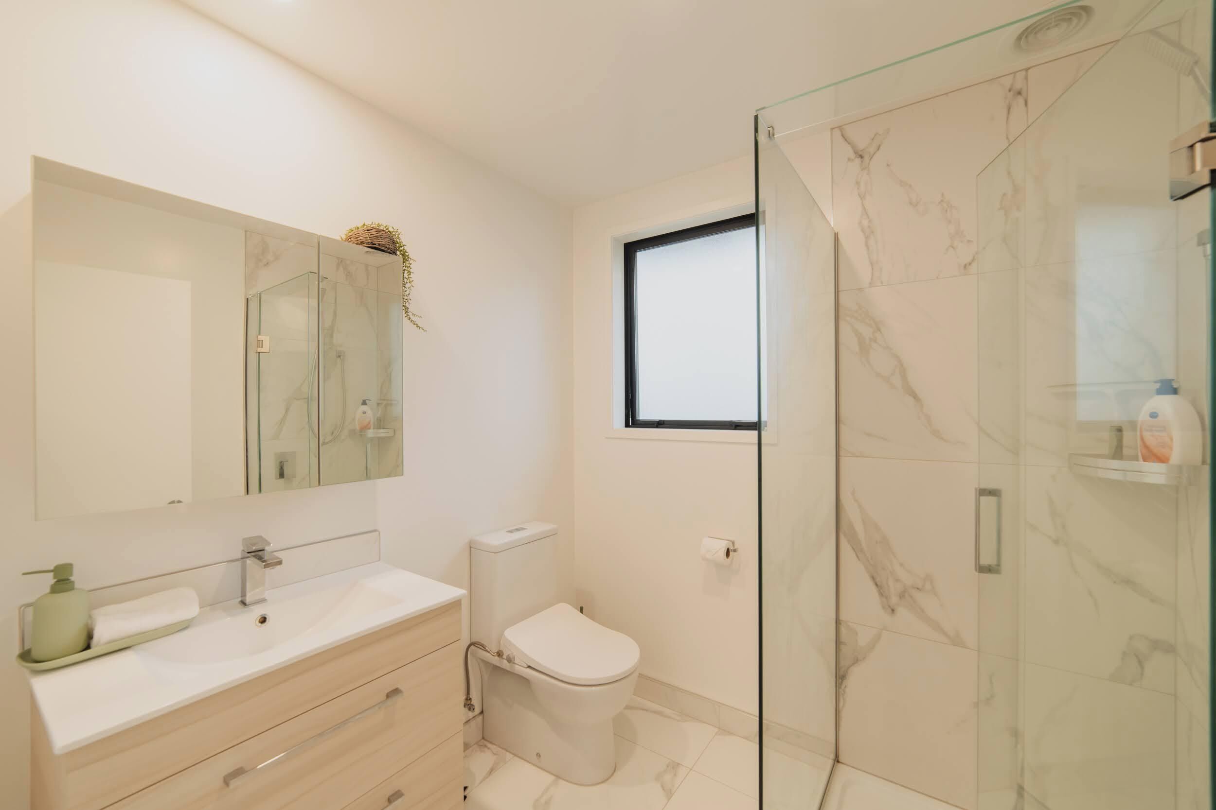 Un baño moderno con cabina de ducha de vidrio, un lavabo blanco con espejo y un inodoro.
