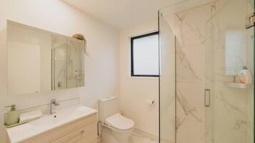 Un baño moderno con cabina de ducha de vidrio, un lavabo blanco con espejo y un inodoro.