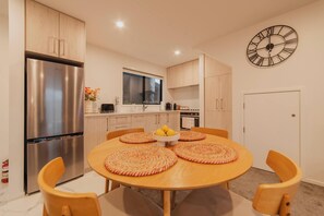 A modern kitchen with a stainless steel refrigerator, wooden cabinets, a round dining table with placemats, and a wall clock.