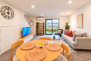 A modern living room with a dining area, a sofa, a TV, and a large window.