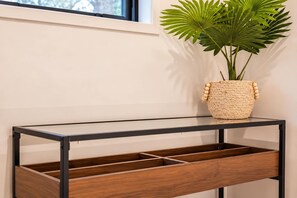 A modern console table with a woven basket containing a plant, positioned next to a window with a view of trees.