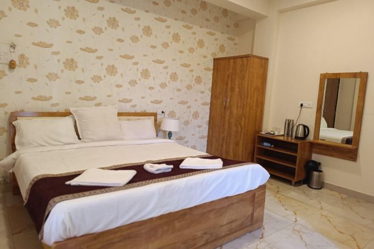 Habitación de hotel con una cama, un armario, un espejo y una mesita con una tetera.