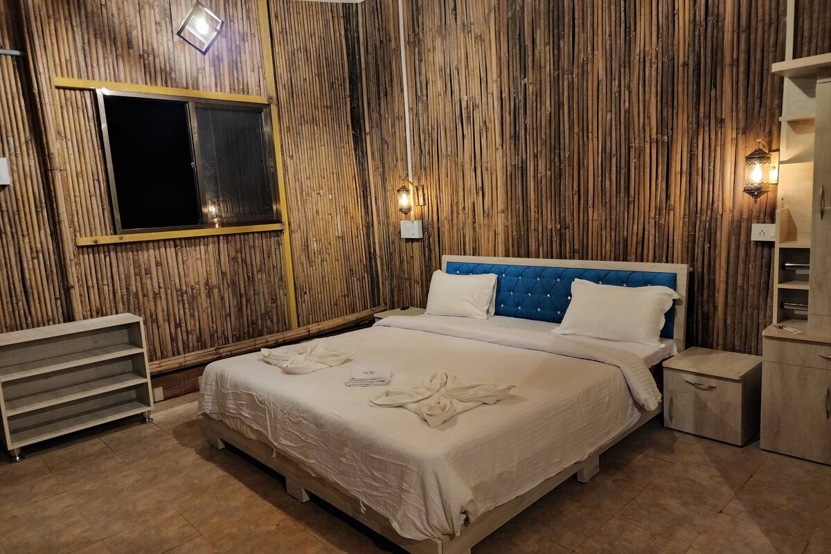 Une chambre avec un grand lit, des murs en bois et deux lampes fixées au mur.