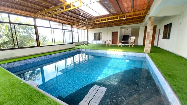 Una piscina interior con techo de azulejos, césped artificial verde y vistas al exterior a través de grandes ventanales.