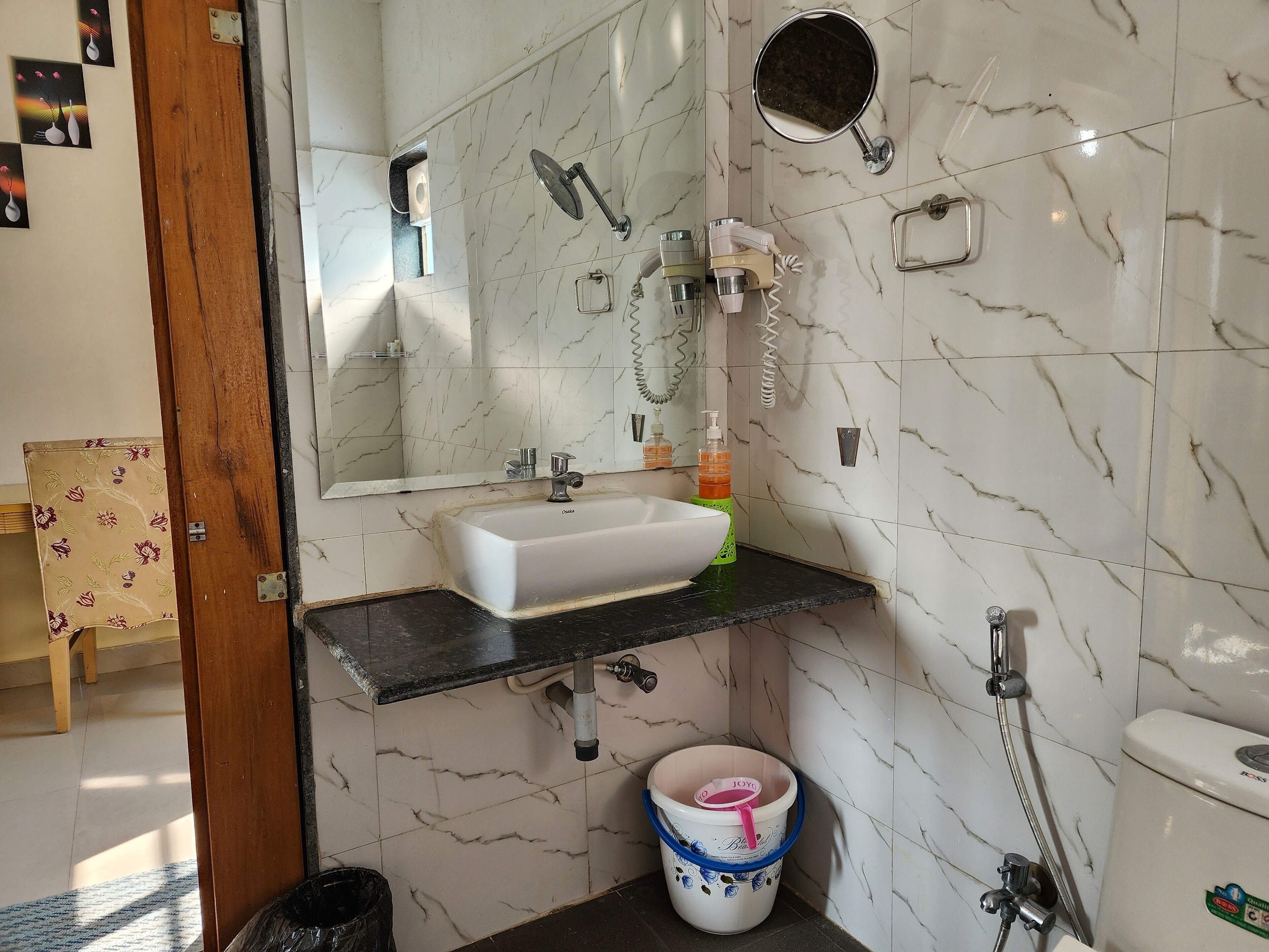 Une salle de bain avec un lavabo blanc, un miroir, une douchette et des toilettes.