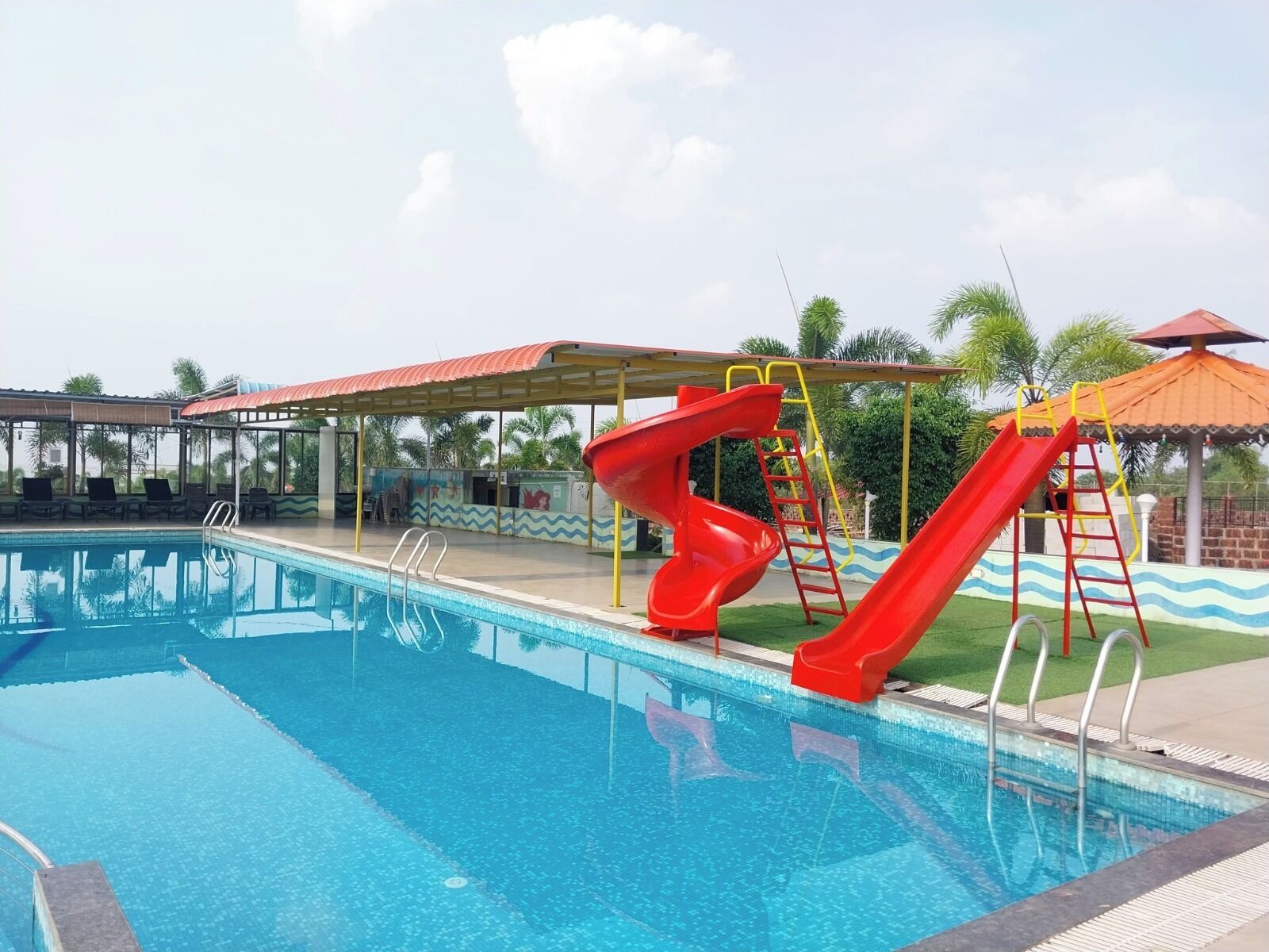 A swimming pool with two red slides and a covered seating area.