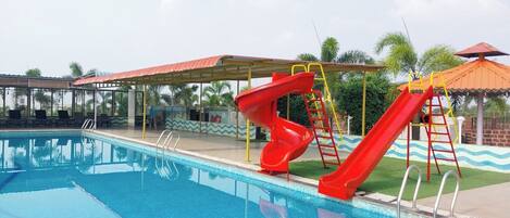 A swimming pool with two red slides and a covered seating area.