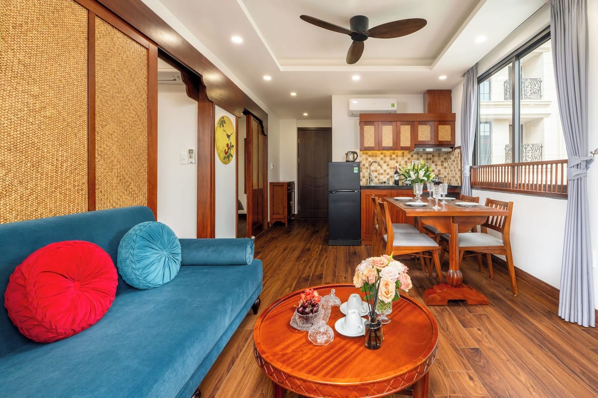 A modern living room with a blue sofa, a wooden dining table, and a ceiling fan.