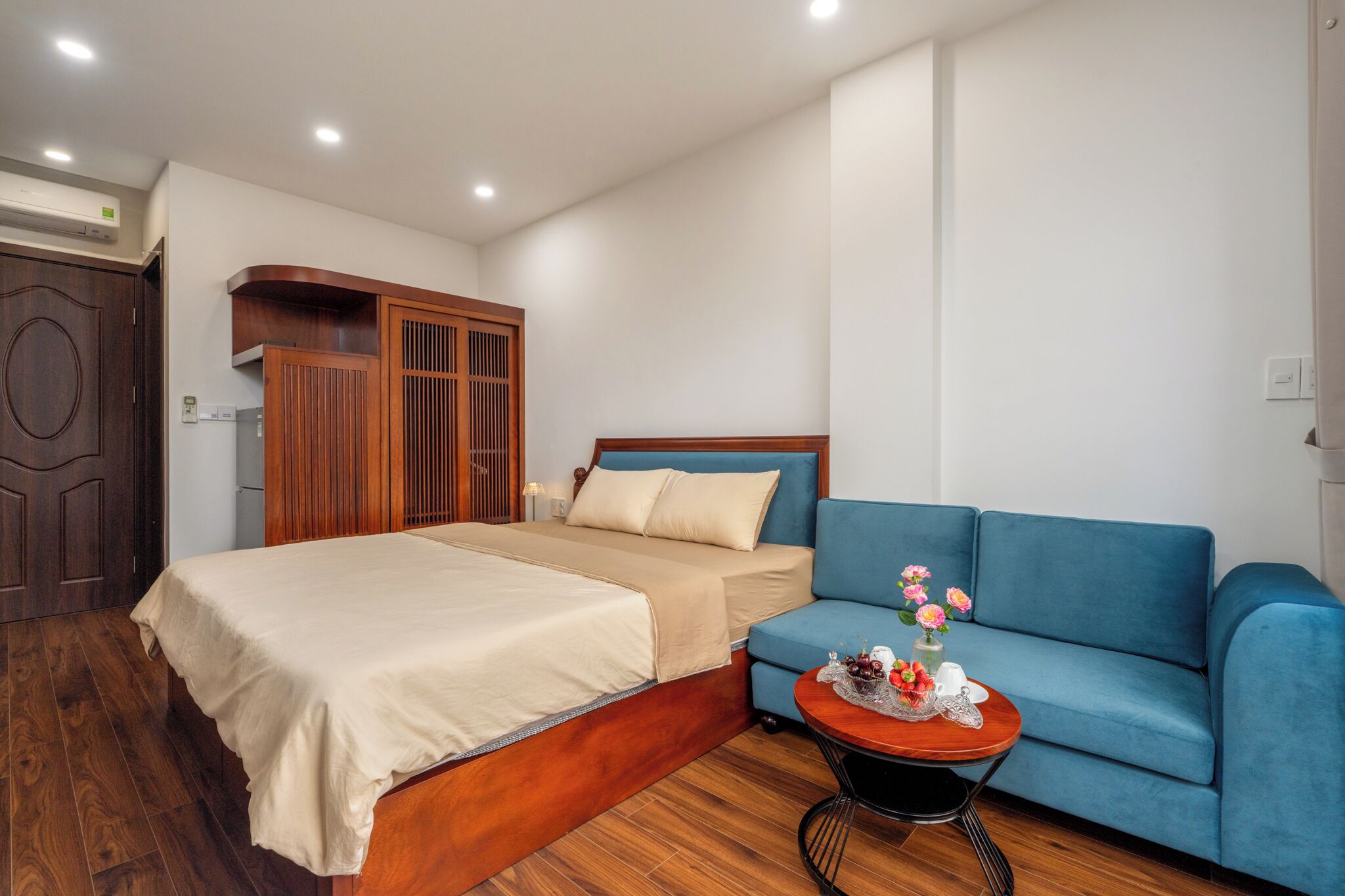 A bedroom with a bed, a blue sofa, a small round table with flowers, and wooden furniture.