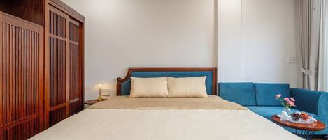 A hotel room with a large bed, a blue sofa, a wooden wardrobe, and a nightstand with a lamp.