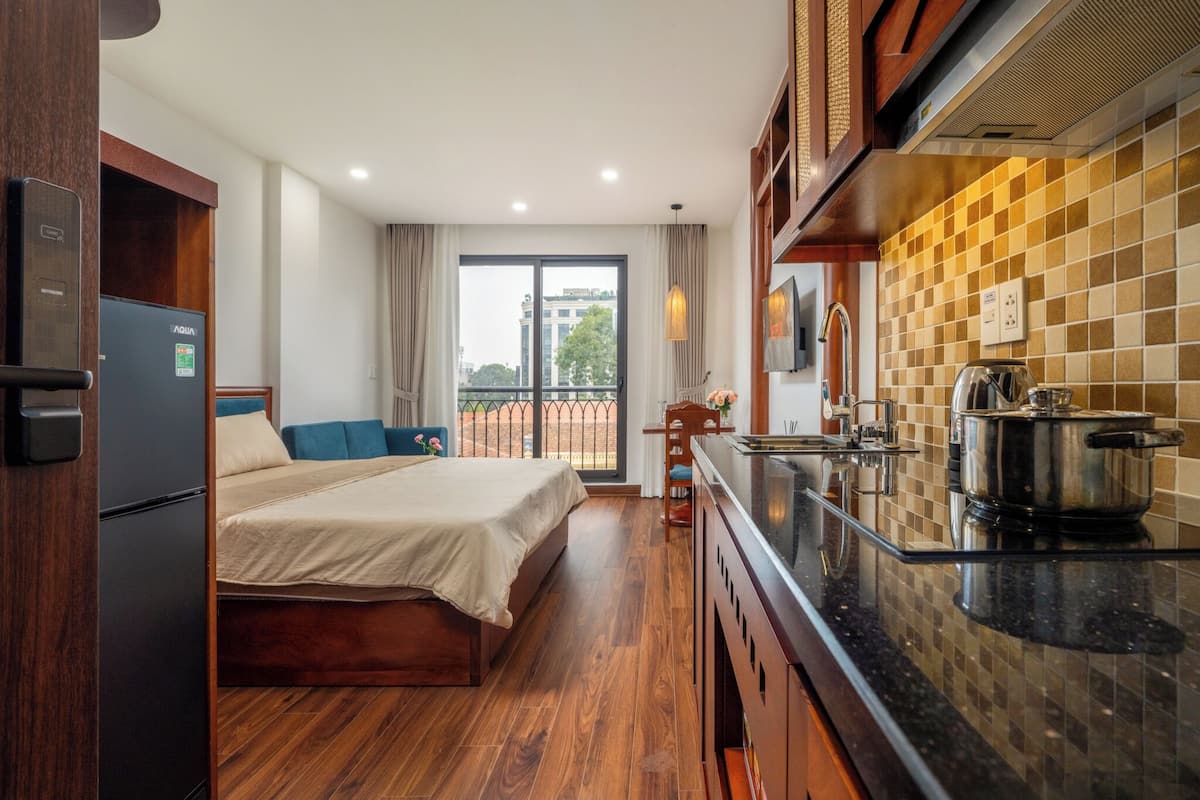 A hotel room with a bed, a kitchenette, a refrigerator, and a view of the outside.