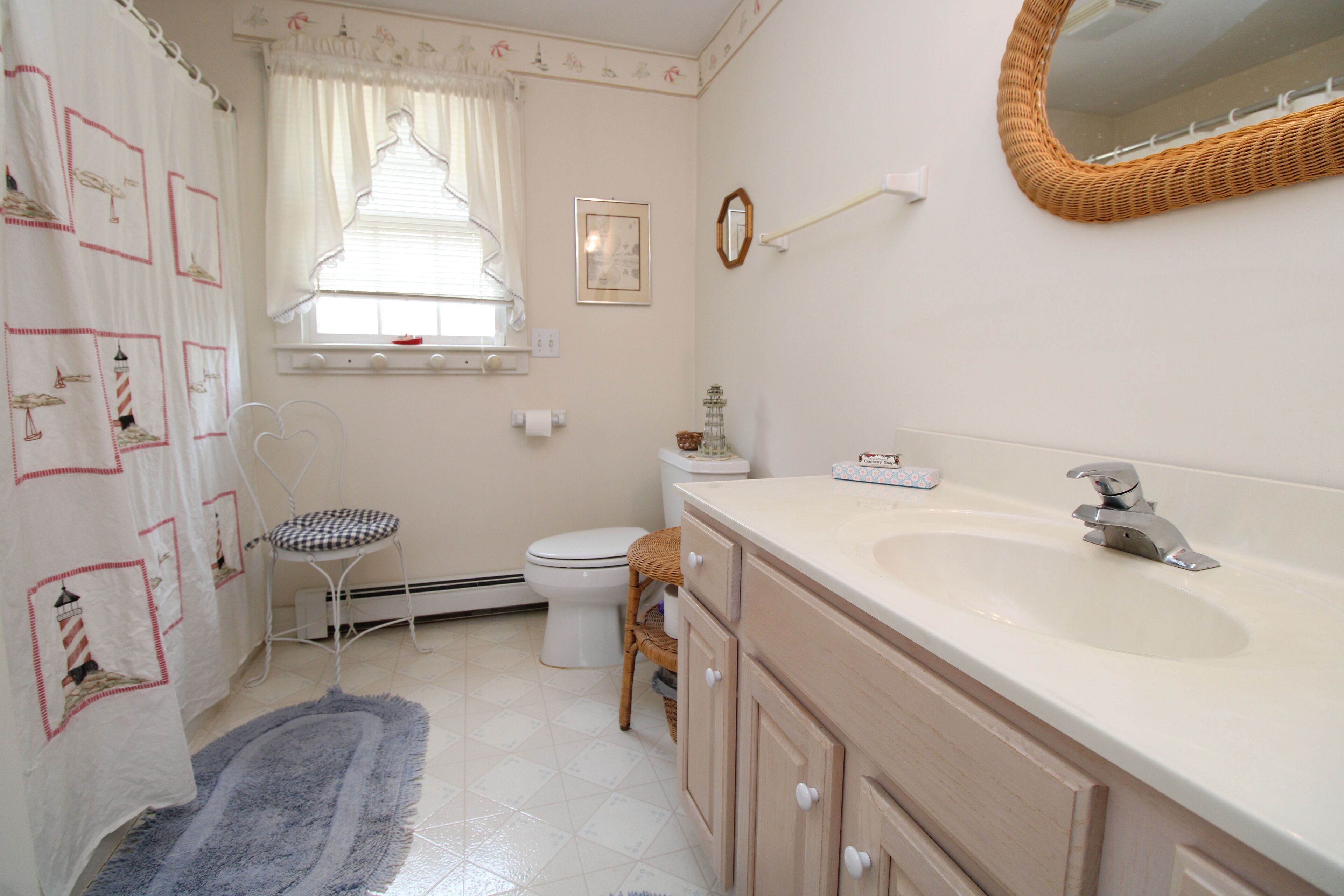 A bathroom with a white sink, a mirror, a toilet, a wicker chair, and a patterned shower curtain.