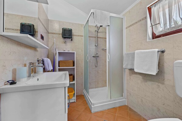 Un baño con ducha de vidrio, lavamanos blanco y retrete.