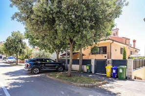 A residential street with a parked SUV, a tree-lined sidewalk, and a house with a gated entrance.