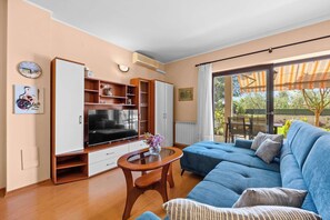 Ein Wohnzimmer mit einer Couch, Fernseher, Holzschrank und einem Glastisch.