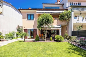 A two-story house with a covered patio, a small garden, and a clear blue sky.