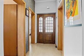 A hallway with wooden doors, a framed picture on the wall, and a tiled floor.
